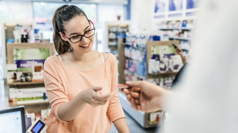 Eine Frau zeigt in einer Apotheke ihre Krankenversichertenkarte vor. 