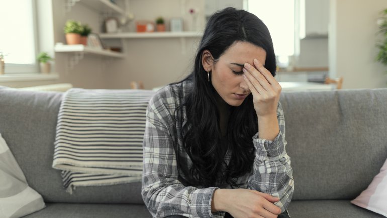 Eine Frau sitzt auf dem Sofa und wirkt niedergeschlagen und traurig.