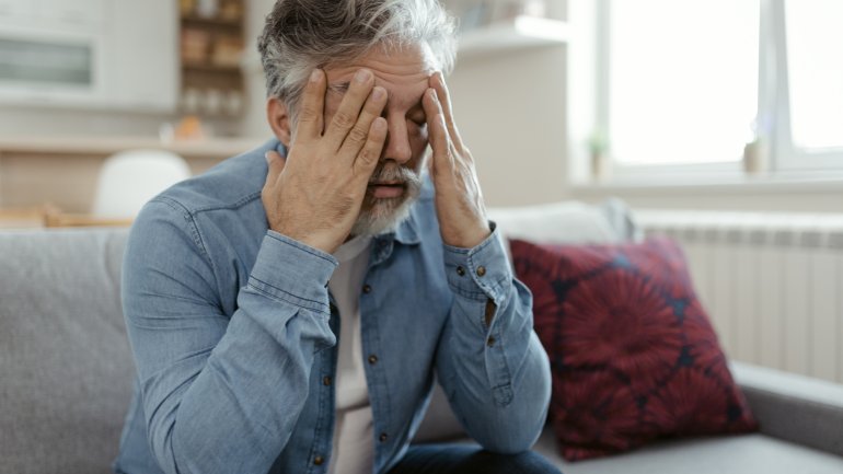 Symbolbild: Mann mit Wernicke-Enzephalopathie sitzt auf Sofa und leidet unter Symptomen.