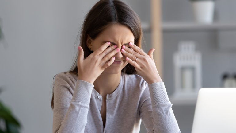 Frau mit Augenmigräne hält sich Hände vor Augen.