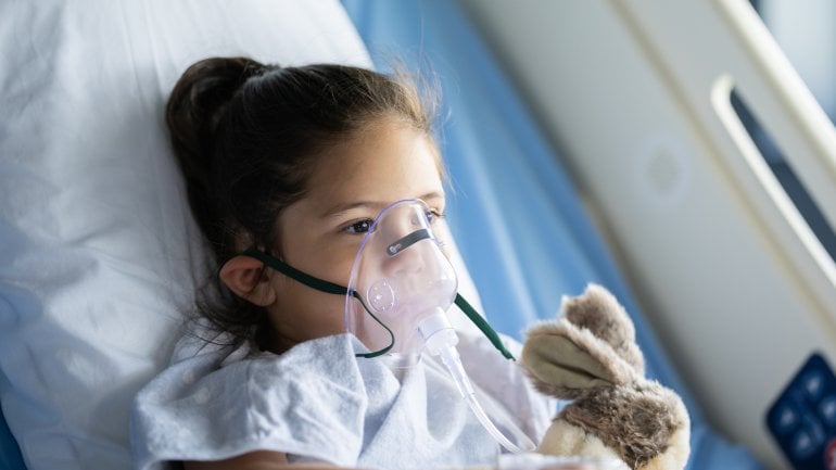 Kind mit RS-Virus liegt im Krankenhaus und trägt eine Sauerstoffmaske.