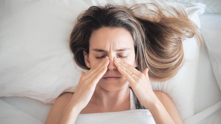 Frau mit Nasennebenhöhlenentzündung liegt im Bett und fasst sich an schmerzende Nebenhöhlen.