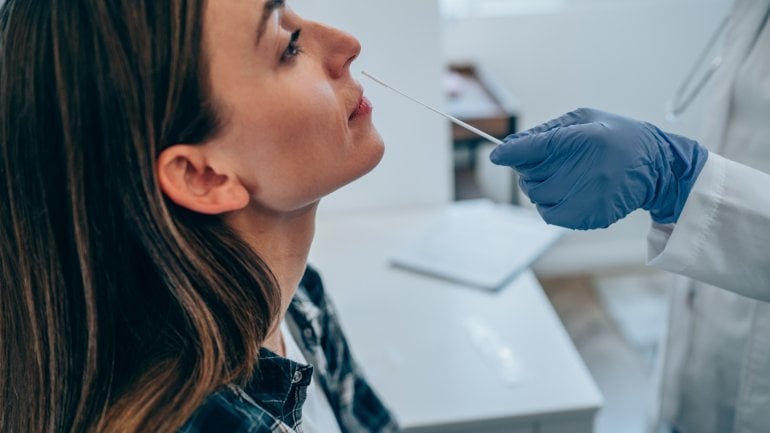 Ein Arzt führt einen PCR-Test bei einer jungen Frau durch.