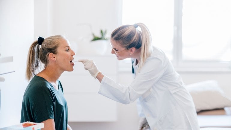 Ärztin untersucht Zunge von blonder Patientin mit Spatel