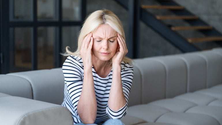 Frau mit Riesenzellarteriitis sitzt auf Sofa und fasst sich an schmerzenden Kopf.