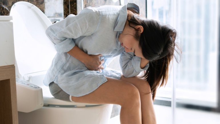 Frau mit Gallensäureverlustsyndrom sitzt auf der Toilette und hat Bauchschmerzen.