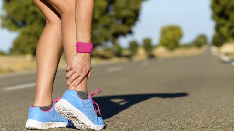 Das Bild zeigt eine Joggerin, die sich ihre Achillessehne hält.