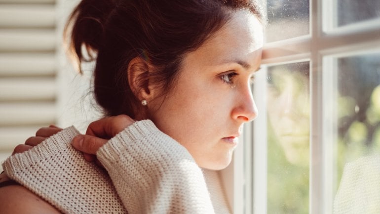 Eine traurig aussehende Frau schaut aus dem Fenster.