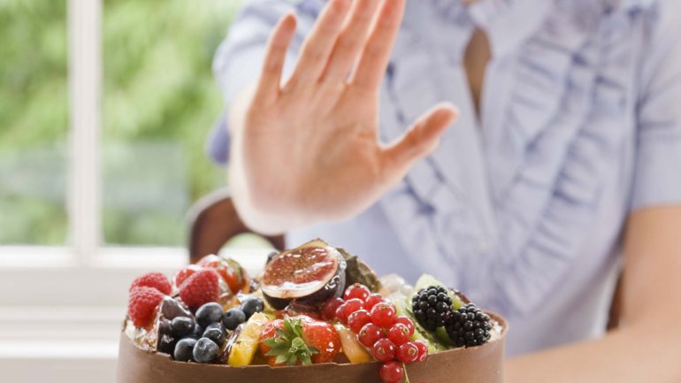 Eine Frau lehnt mit einer Handbewegung das ihr angebotene Essen ab.