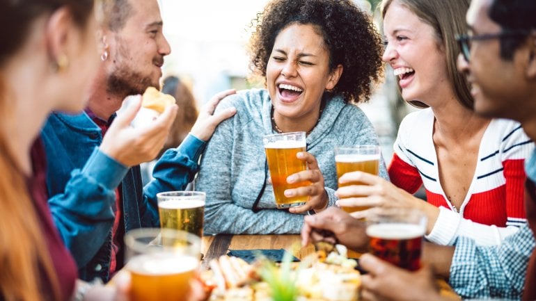 Freund sitzen im Biergarten zusammen, lachen und stoßen mit Bier an