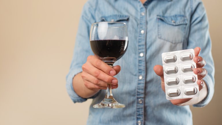 Ein Mann hält ein Glas wein und eine Packung Antibiotika vor sich