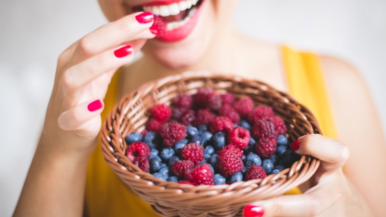 Eine Frau isst aus einer Schüssel voller Blaubeeren und Himbeeren