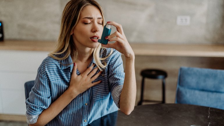 Frau mit Asthma bronchiale fasst sich an Brust und wendet Spray an.