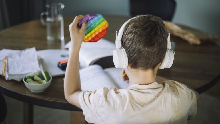 Kind mit Autismus sitzt am Schreibtisch, hört Musik und macht Hausaufgaben.
