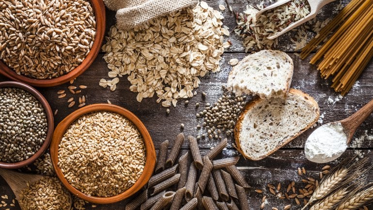 Tisch mit verschiedenen Vollkornprodukten wie Haferflocken, Nudeln und Brot