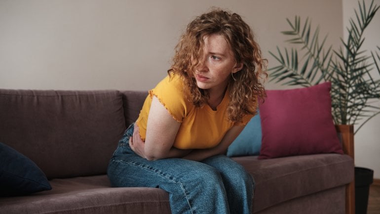 Eine junge Frau sitzt auf dem Sofa und hält sich den schmerzenden Bauch