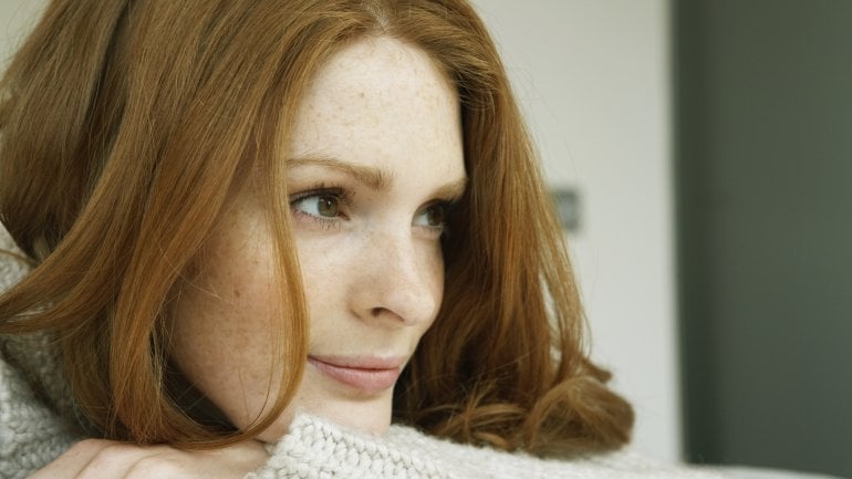 Das Bild zeigt eine Frau mit Sommersprossen und roten Haaren.