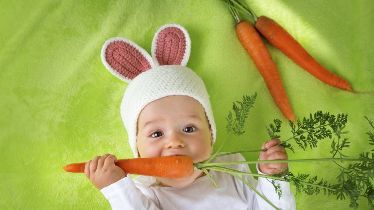 Ein Baby im Hasenkostüm knabbert an Möhren.