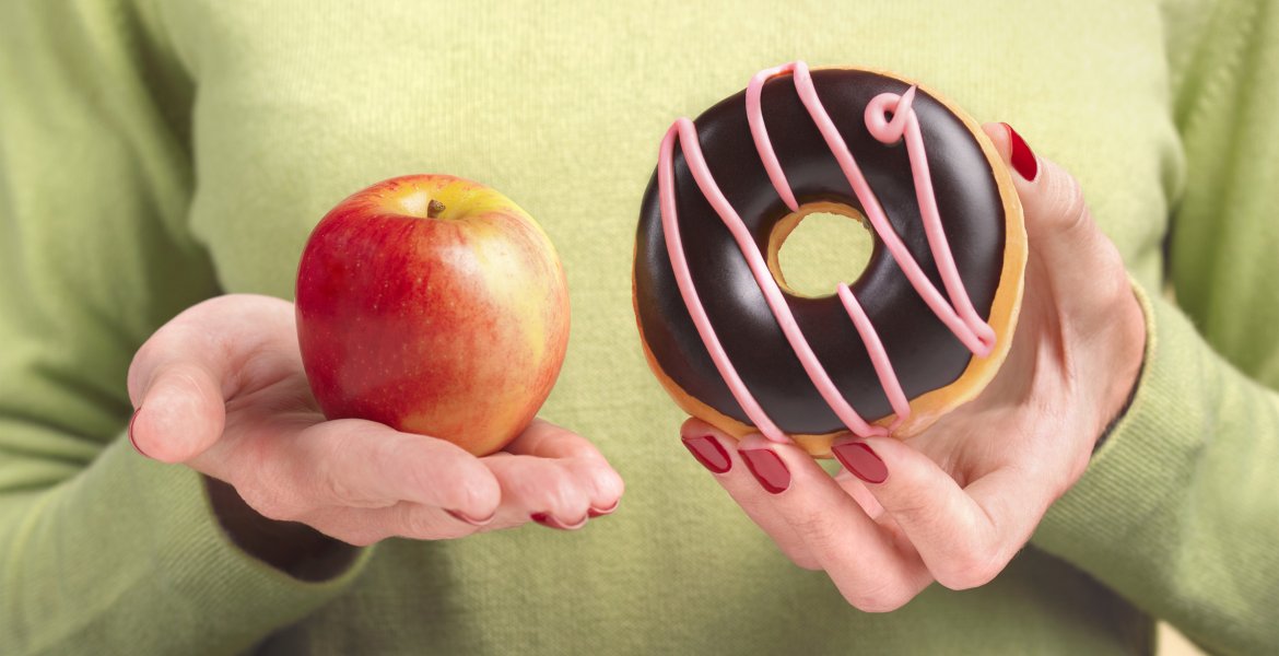 Eine Frau hält in der einen Hand einen Apfel, in der anderen einen Donut