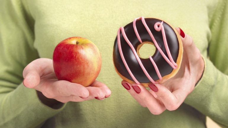 Eine Frau hält in der einen Hand einen Apfel, in der anderen einen Donut