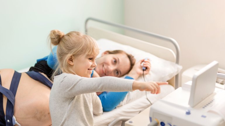 Das Bild zeigt ein Mädchen mit seiner Mutter, die an ein Gerät zur Messung der CTG-Werte angeschlossen ist.