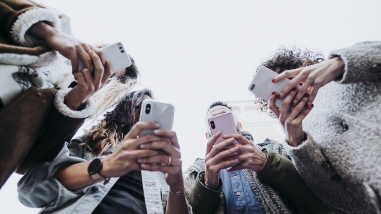 Mehrere junge Leute stehen zusammen und beschäftigen sich mit ihren Smartphones.