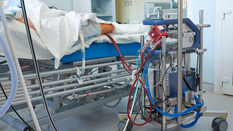 Man sieht einen Intensivpatienten im Bett, daneben eine ECMO