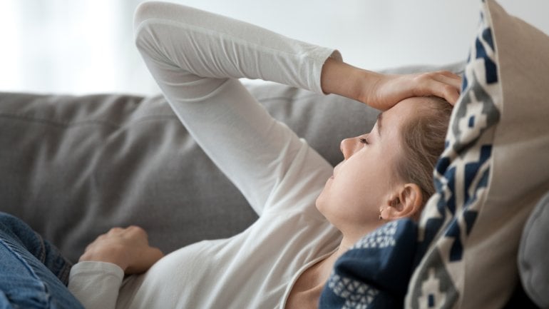 Eine Frau liegt auf dem Sofa und hält sich den Kopf.