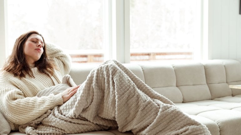 Frau mit blasser Haut aufgrund einer Eisenmangelanämie liegt müde auf dem Sofa.