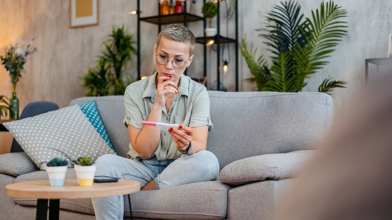 Eisprung: Eine Frau sitzt mit einem Schwangerschaftstest auf dem Sofa.