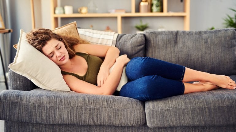 Frau mit Endometriose liegt auf dem Sofa und hat Schmerzen.