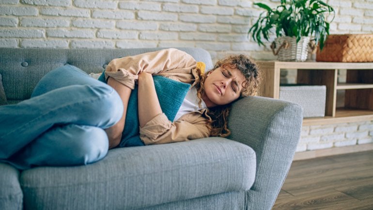 Frau mit Endometriose liegt auf dem Sofa und hat starke Schmerzen im Unterleib.