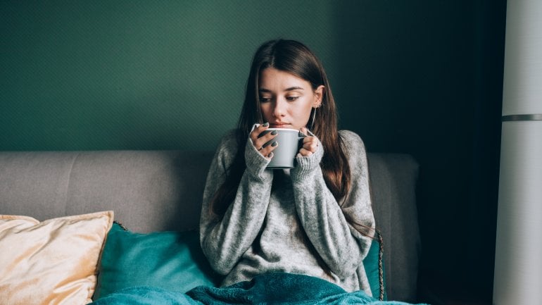 Eine verschnupfte Frau liegt auf dem Bett