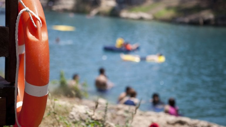 Man sieht einen Rettungsring und im Hintergrund einen Badesee.