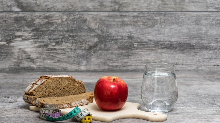 Holzbrett mit Wasserglas, Brot, Apfel und Maßband