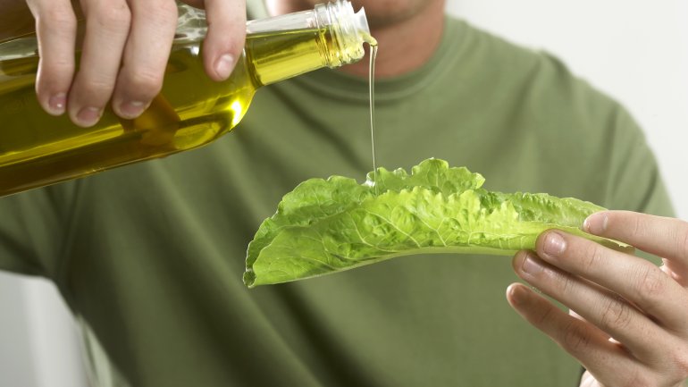 Das Bild zeigt einen Mann, der Öl auf ein Salatblatt gießt. 