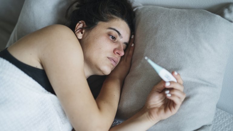 Frau mit Fleckfieber hat Thermometer in der Hand und liegt im Bett.