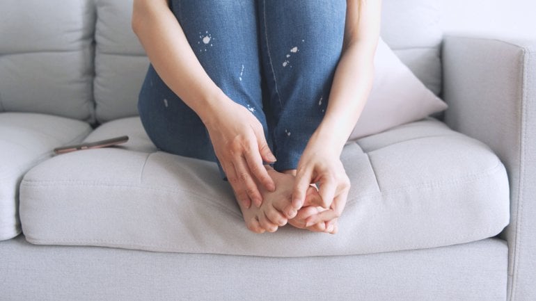 Eine Frau sitzt mit angezogenen Beinen auf dem Sofa.