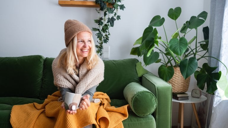 Frierende Frau warm angezogen auf dem Sofa.