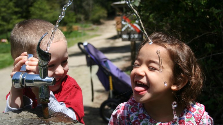 Zwei Kindern trinken an einem Wasserspender.