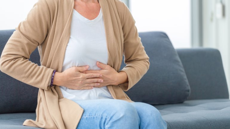 Frau mit Gallensteine fasst sich an den Oberbauch und sitzt auf dem Sofa.