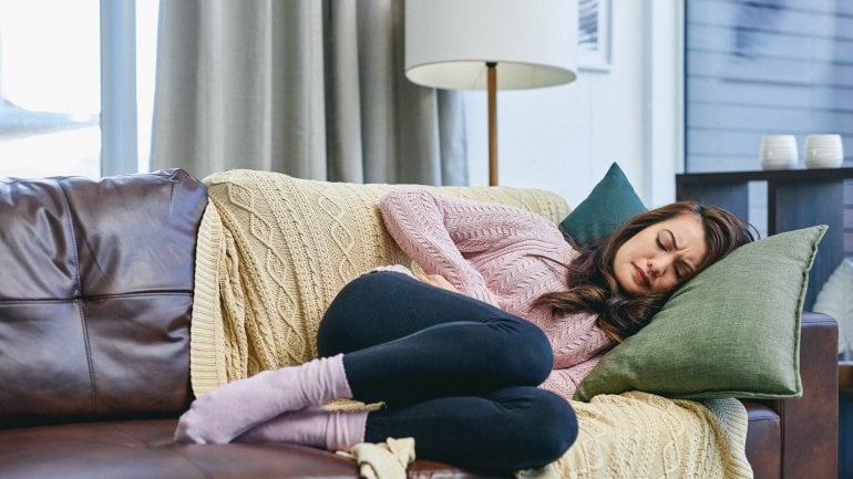 Frau liegt auf dem Sofa und leidet unter einer Gebärmutterentzündung.