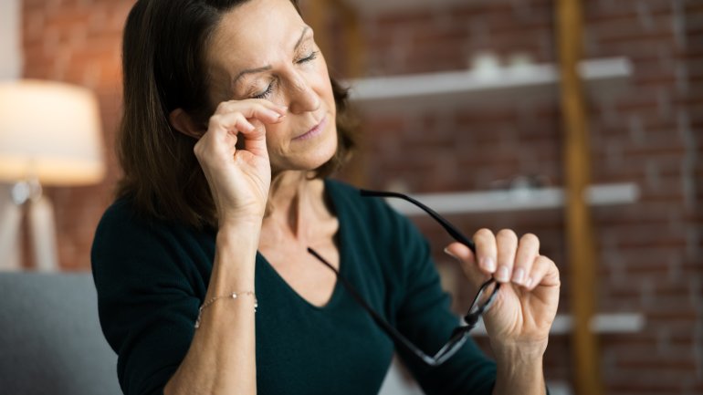 Frau mit Gerstenkorn fasst sich an schmerzendes Auge.