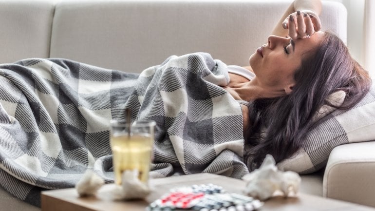Eine Frau liegt mit Grippe auf dem Sofa