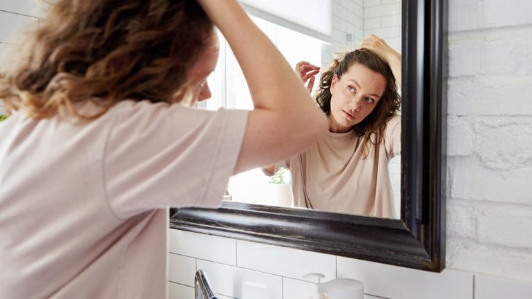 Hormoneller Haarausfall: Eine Frau prüft ihre Haare vor dem Spiegel