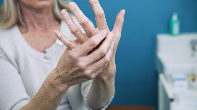 Eine Frau umfasst ihre linke mit der rechten Hand.