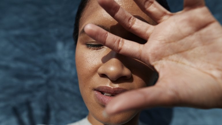 Frau mit Symptomen eines Hitzschlags steht in der Sonne.