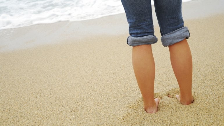 Eine Person steht barfuß am Strand.