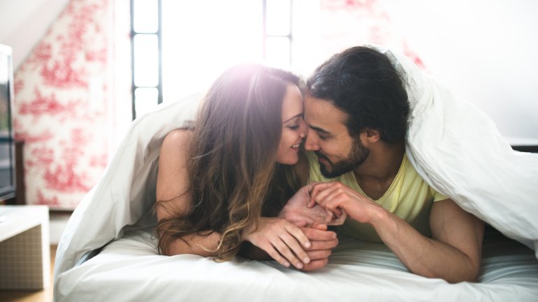 Eine Frau und ein Mann liegen bäuchlings im Bett und schmusen miteinander.