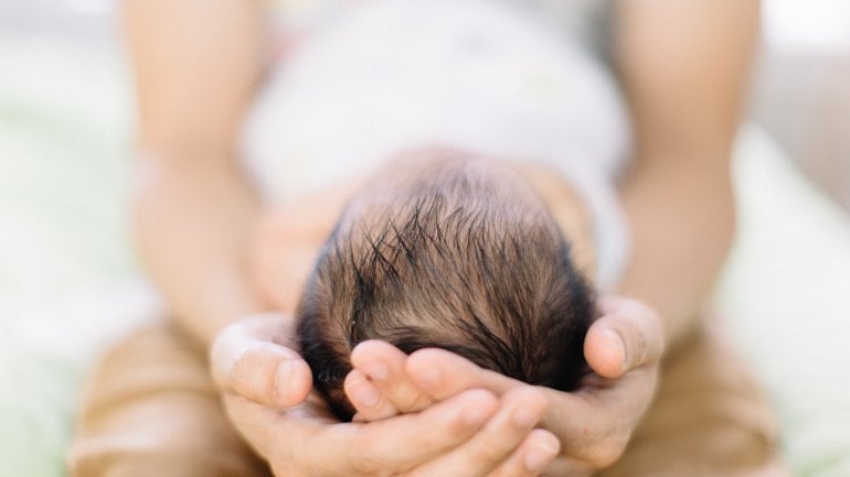 Hände halten den Kopf eines Babys